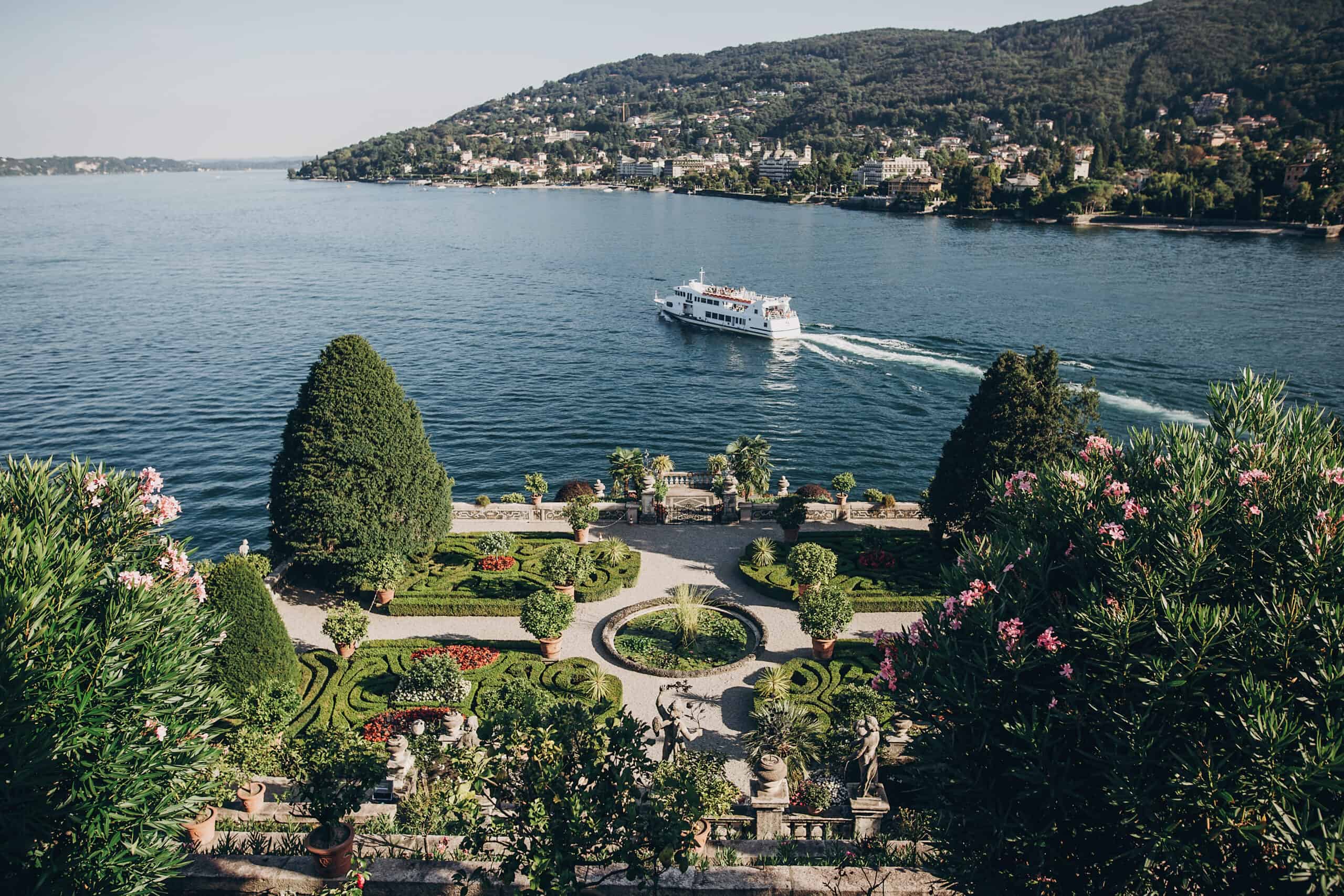 Beautiful view of stone landmarks and green terrace with flowers at  Lago Maggiore with ships and boats, exploring  Borromean Islands, Italy. Exploring old architecture monuments in Stresa